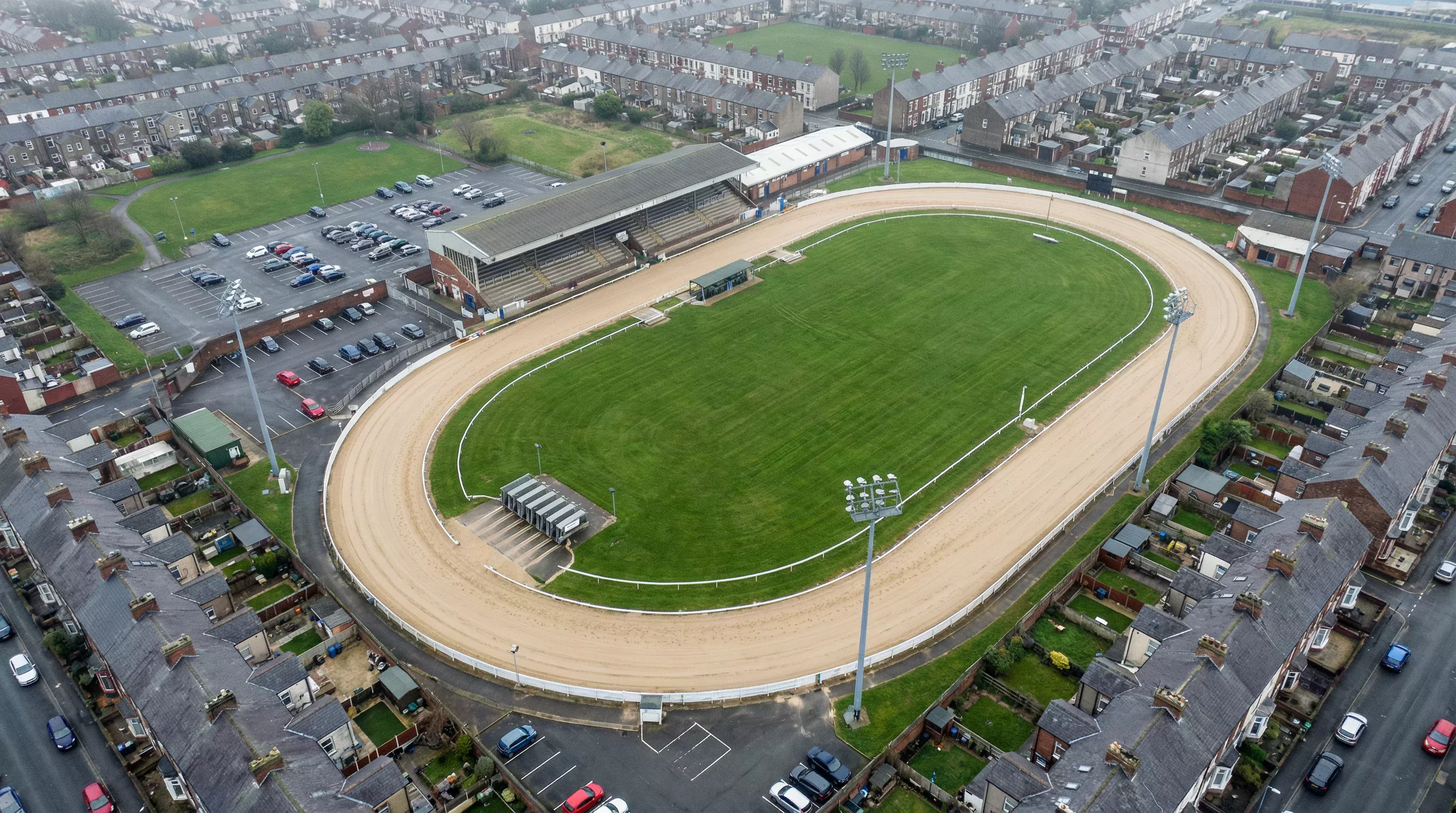 UK greyhound results by track — aerial view of a licensed greyhound stadium with oval sand track and floodlit stands